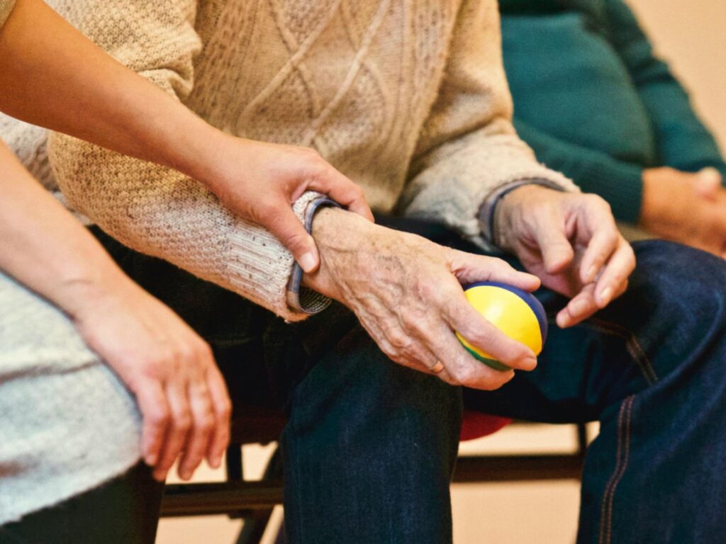 Caregiver supporting an elderly person’s hand during a stress ball exercise, representing rehabilitation and home care services in San Francisco
